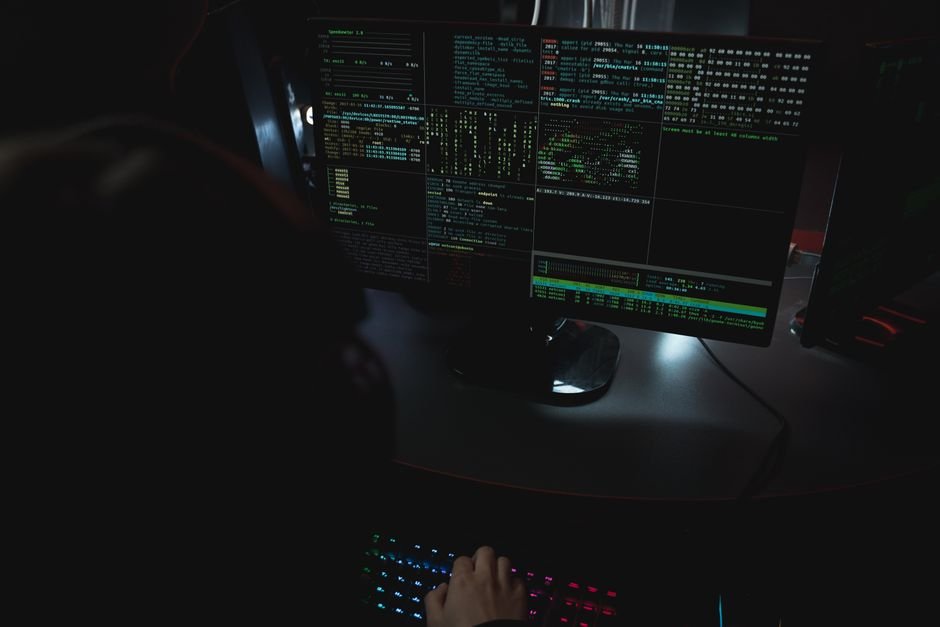 Dark room with code on monitors, representing cybersecurity work taught at the top universities in USA for cybersecurity